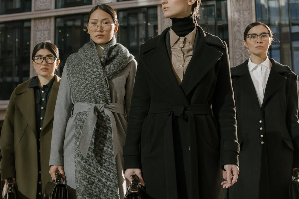A group of fashionable women in coats standing confidently in an urban environment.